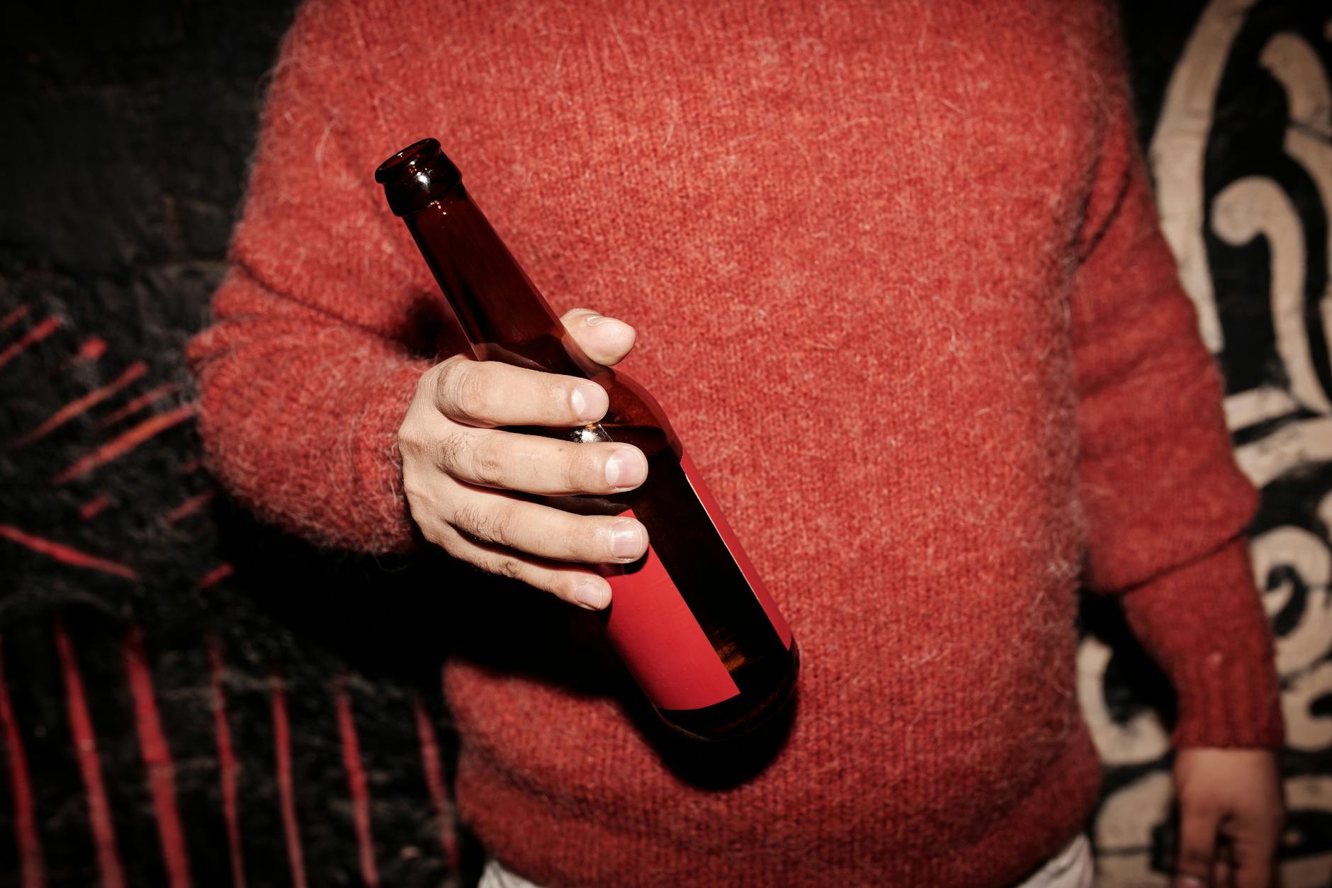Osoba w czerwonym swetrze z butelką piwa przy fakturowanej ścianie
