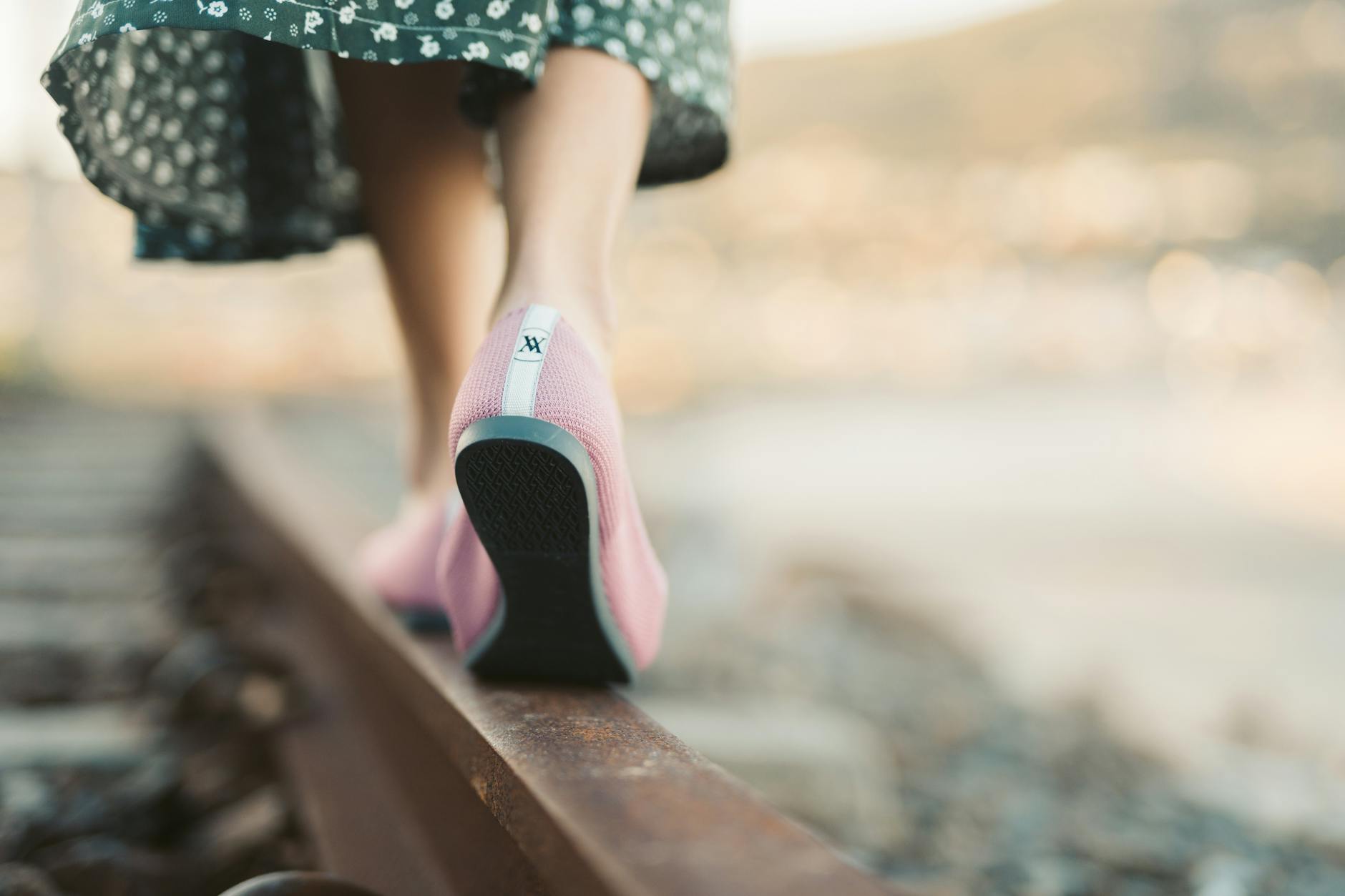 Kobieta w letniej sukience i różowych butach idzie po torach kolejowych