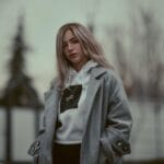 Blondynka w płaszczu i sportowej bluzie pozuje na zimowej ulicy