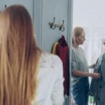 Dwie kobiety mierzą płaszcze w butiku, wybierając odpowiedni materiał