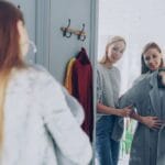 Dwie kobiety mierzą płaszcze w eleganckim butiku z lustrem