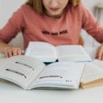 Kobieta w różowej bluzce uczy się przy kilku otwartych książkach