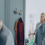 Kobieta w sklepie przymierza płaszcz, obserwując się w lustrze