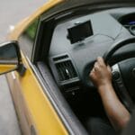 Kierowca prowadzący żółtą taksówkę z nawigacją GPS w ruchu miejskim