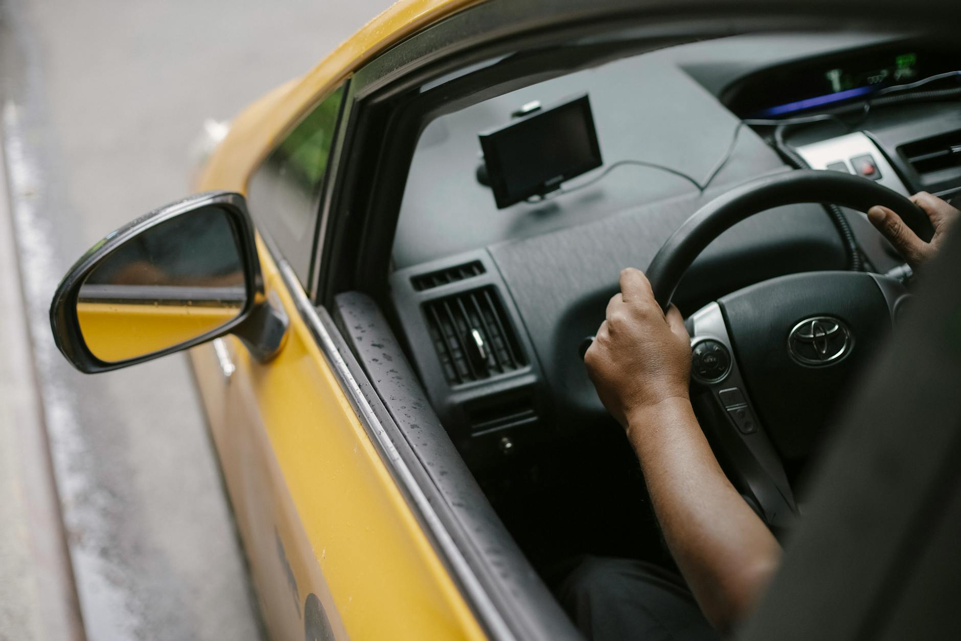 Kierowca prowadzący żółtą taksówkę z nawigacją GPS w ruchu miejskim Kierowca prowadzący żółtą taksówkę z nawigacją GPS w ruchu miejskim