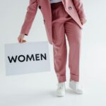 Kobieta w różowym garniturze trzyma kartkę z napisem WOMEN