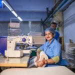Krawcowa szyjąca ubranie na maszynie w jasnej hali produkcyjnej