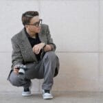 Młody fotograf w garniturze w sneakersach kuca z aparatem vintage