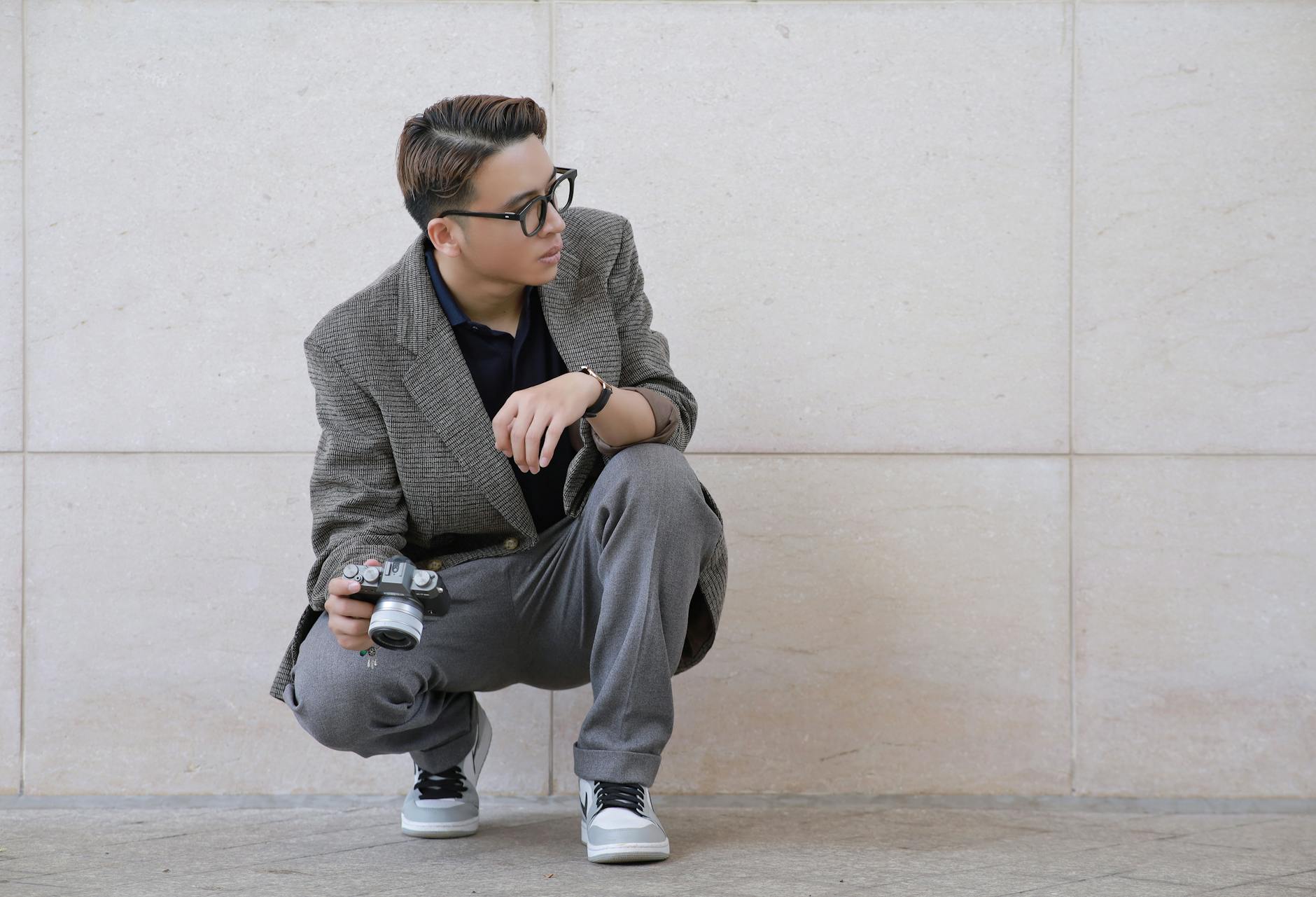Młody fotograf w garniturze w sneakersach kuca z aparatem vintage