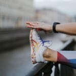 Osoba rozciąga nogę w kolorowych butach przy kanale w mieście