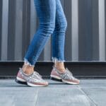 Kobieta w dżinsach idzie chodnikiem w modnych miejskich sneakersach