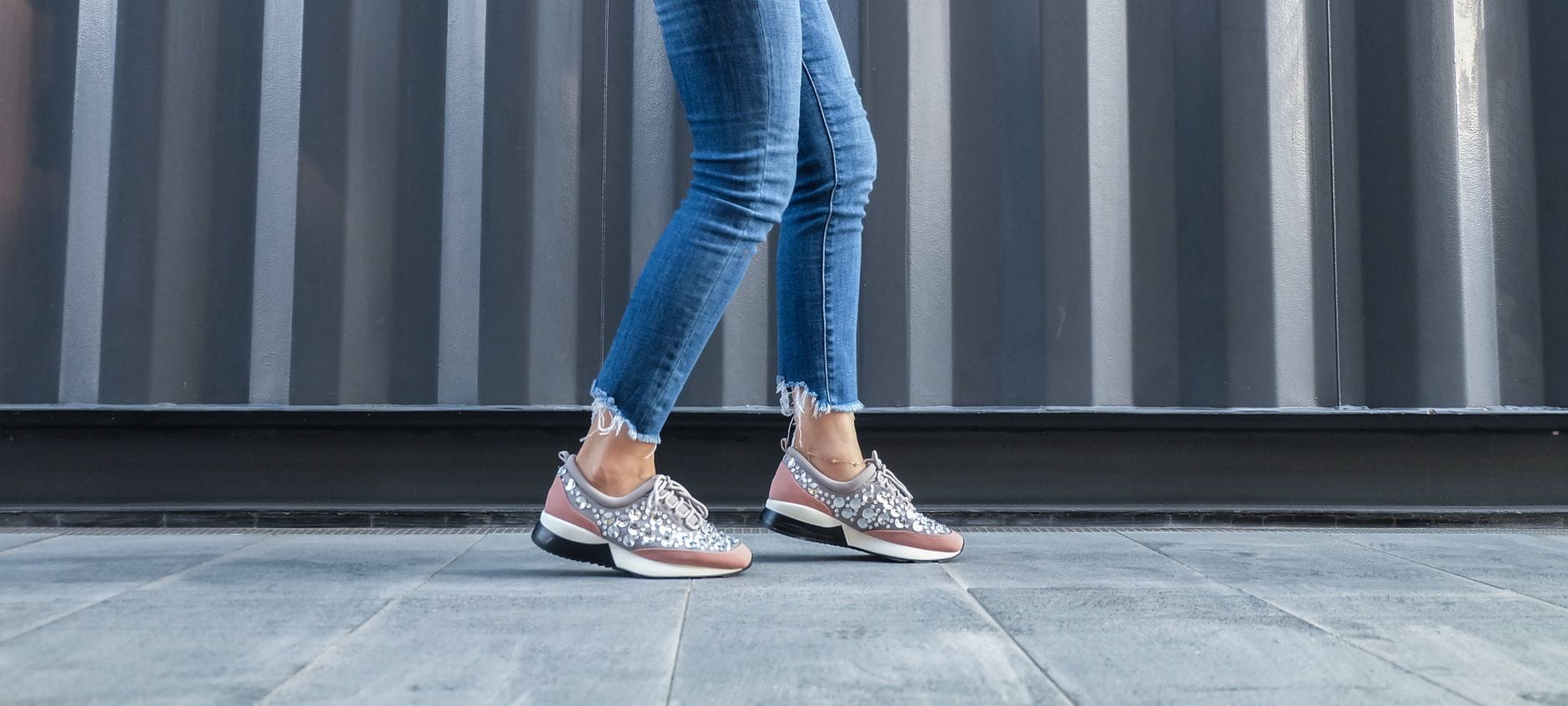 Kobieta w dżinsach idzie chodnikiem w modnych miejskich sneakersach Kobieta w dżinsach idzie chodnikiem w modnych miejskich sneakersach